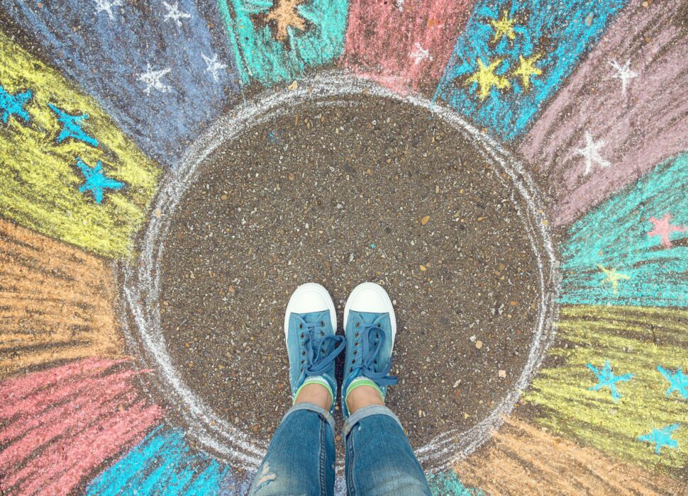 Comfort zone concept. Feet standing inside comfort zone circle surrounded by rainbow stripes painted with chalk on the asphalt.