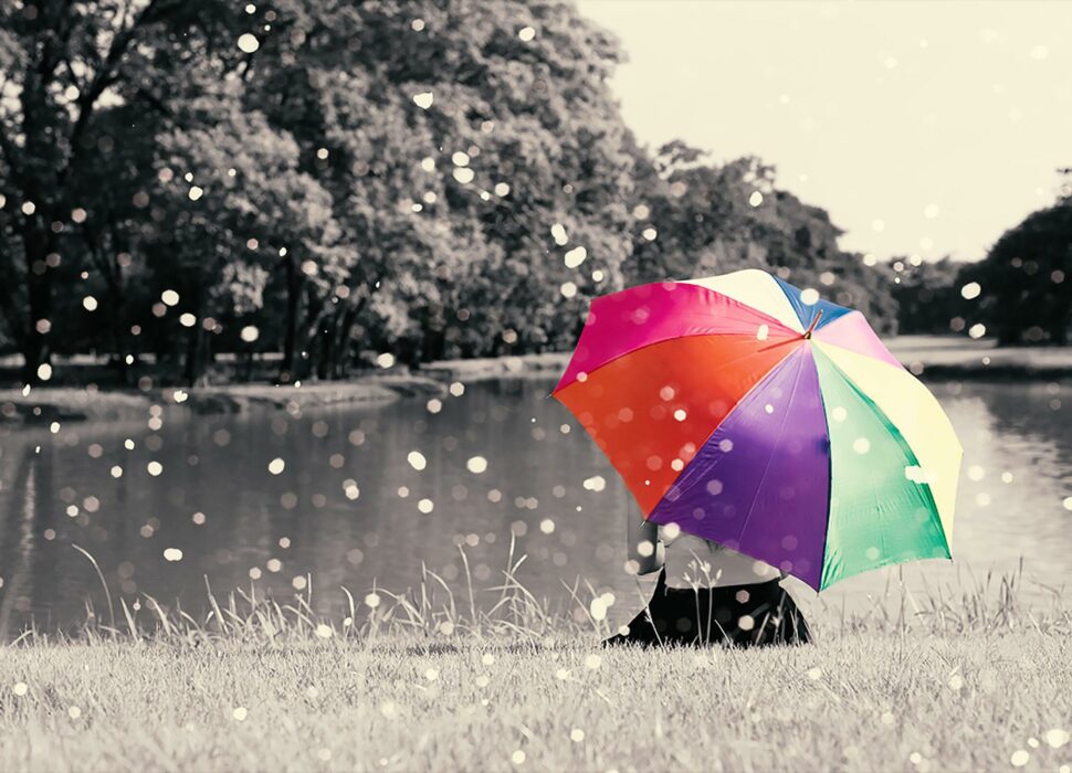 Colorful rainbow umbrella hold by sitting woman on grass field near river at outdoor with full of nature and rain, Relax concept, Beauty concept, Lonely concept, selective color, Sepia dramatic tone