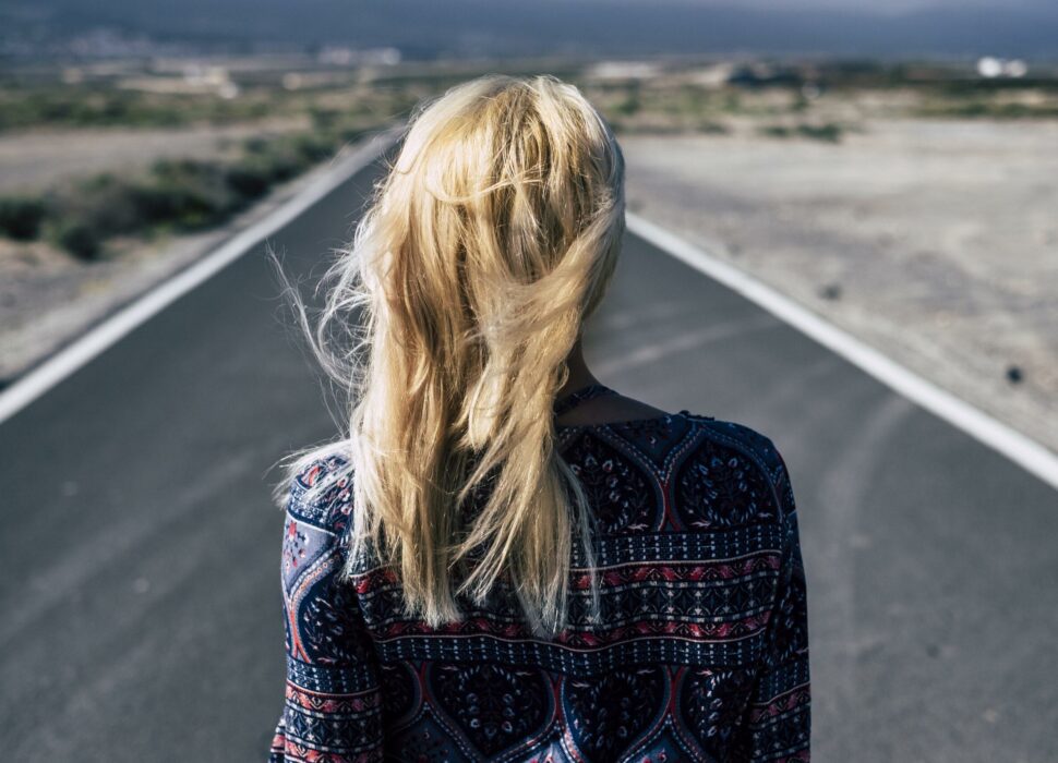 Blonde young girl viewed from rear walk on a long straight road in the country side. Decisions and future concept for millennial people looking for a job or a way to happiness - freedom and fear